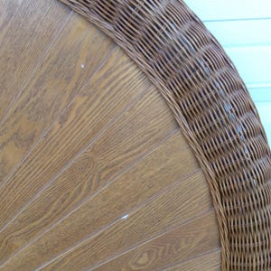 May include: Close-up of a section of a brown wicker chair back. The chair back has a wooden panel design with a woven wicker border. The wood has a light brown color with visible wood grain.