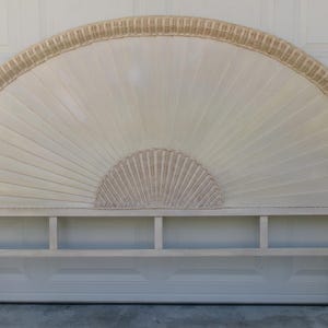 May include: Off-white, fan-shaped headboard with a woven rattan border and center detail. The headboard has a rectangular base with vertical supports. The design features a sunburst pattern, adding a touch of vintage charm to bedroom decor.