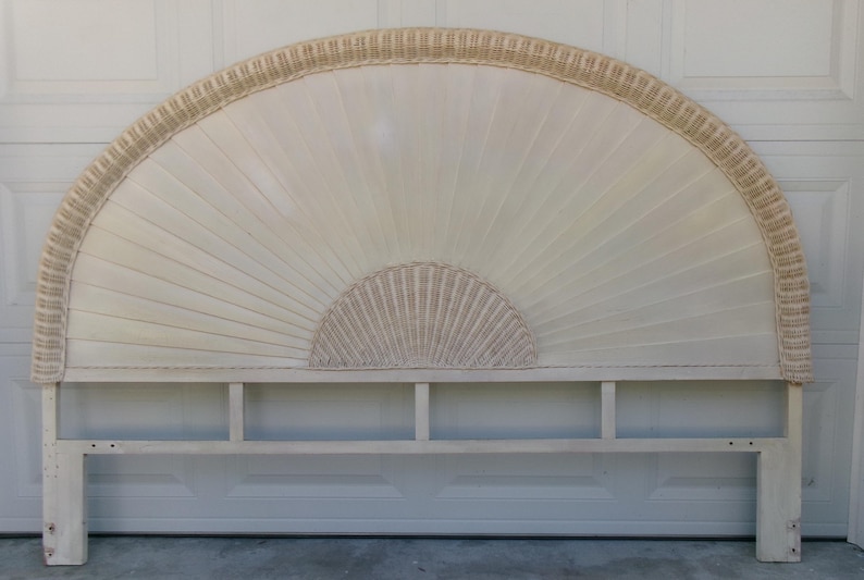 May include: Off-white, fan-shaped headboard with a woven rattan border and center detail. The headboard has a rectangular base with vertical supports. The design features a sunburst pattern, adding a touch of vintage charm to bedroom decor.