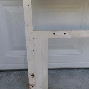 May include: A section of a white-painted wooden headboard frame with a woven wicker top. The frame has visible screw holes and some wear. The headboard is designed for a bed.