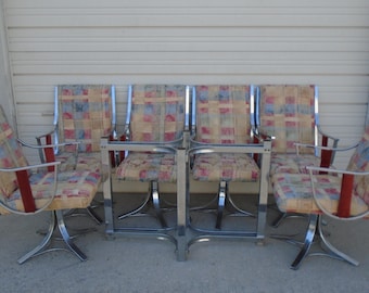 May include: Set of six vintage chairs with chrome frames and patterned fabric seats. The chairs have a swivel base and armrests with red accents. The fabric features a colorful, geometric design.