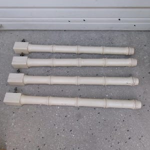 May include: Four off-white, bamboo-style furniture legs. Each leg has a square top and a cylindrical body with carved details resembling bamboo stalks. The legs are arranged on a gray surface.