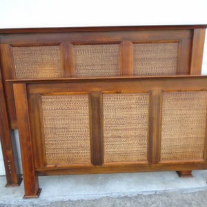 May include: A wooden bed frame with a headboard and footboard. The frame is a warm brown color with woven rattan panels. The headboard is taller than the footboard. The bed frame is made of solid wood and has a classic design.