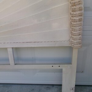 May include: A white painted headboard with a fan-shaped design and woven wicker trim. The headboard has a rectangular base and is made of wood. The headboard is painted in a light, neutral color.