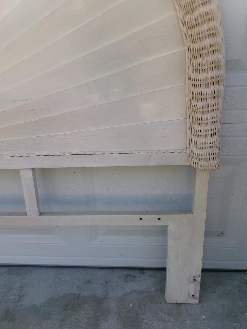 May include: A white painted headboard with a fan-shaped design and woven wicker trim. The headboard has a rectangular base and is made of wood. The headboard is painted in a light, neutral color.
