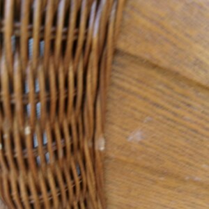 May include: Close-up of a section of a woven wicker chair back. The wicker is a warm brown color, with a textured surface. The chair back is curved and appears to be part of a larger piece of furniture.