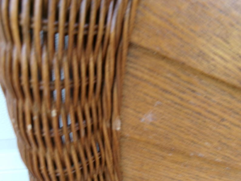 May include: Close-up of a section of a woven wicker chair back. The wicker is a warm brown color, with a textured surface. The chair back is curved and appears to be part of a larger piece of furniture.