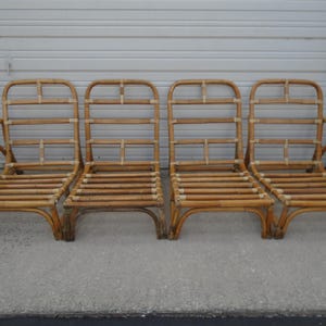May include: Four brown wicker chairs with a simple design. The chairs have a curved back and arms, and are made of woven rattan.