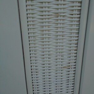 May include: Close-up of a section of a white woven wicker pattern. The wicker is tightly woven, creating a textured surface. The frame is a light gray color, and the wicker is a creamy white.