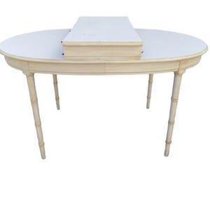 May include: An oval-shaped table with a light cream-colored finish and four legs featuring a bamboo-style texture. A rectangular, light-colored box with a flat top is positioned centrally on the surface of the table, which has a smooth, light-colored top.