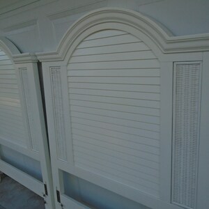 May include: Two off-white headboards with arched tops and horizontal slat detailing. Each headboard features a woven panel on the side. The headboards are made of wood and have a classic design.