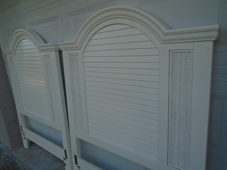May include: Two off-white headboards with arched tops and horizontal slat detailing. Each headboard features a woven panel on the side. The headboards are made of wood and have a classic design.