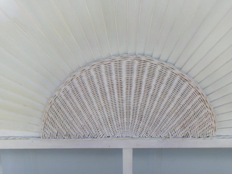 May include: A white, semi-circular wicker headboard with a woven pattern. The headboard is mounted on a white frame and set against a backdrop of white, slatted wood. The design evokes a coastal or bohemian aesthetic.