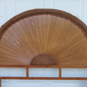 May include: A wooden headboard with a fan-shaped design. The headboard features a woven rattan border and a central panel with a wood grain pattern. The base is made of wood and has a rectangular shape.