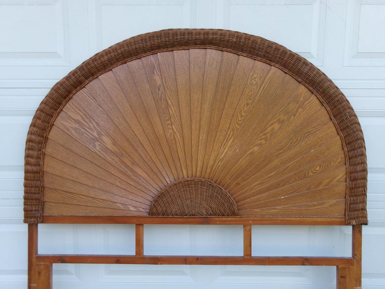 May include: A wooden headboard with a fan-shaped design. The headboard features a woven rattan border and a central panel with a wood grain pattern. The base is made of wood and has a rectangular shape.