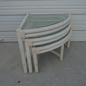 May include: White wicker corner table with three glass shelves. The table is made of woven wicker and has a rounded shape.