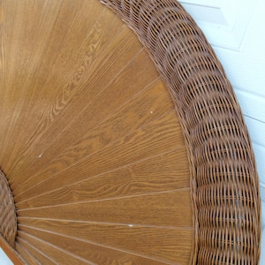 May include: A round, wooden headboard with a woven wicker border. The headboard has a light brown, fan-like design with a woven wicker border. The wood grain is visible, and the wicker is a darker brown.