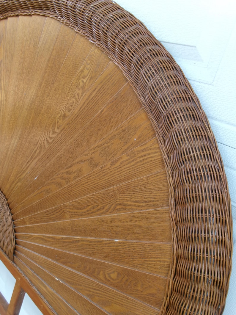 May include: A round, wooden headboard with a woven wicker border. The headboard has a light brown, fan-like design with a woven wicker border. The wood grain is visible, and the wicker is a darker brown.