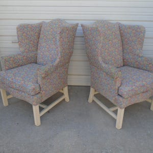 Puede incluir: Un par de sillones de orejas con tapicería de estampado floral y patas de madera pintadas de blanco.