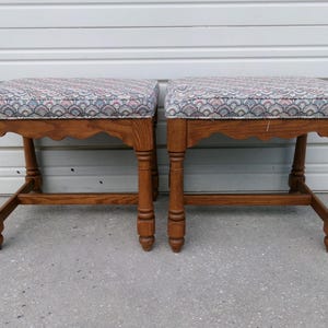 May include: A pair of wooden stools with turned legs and scalloped aprons. Each stool features a rectangular seat upholstered in a fabric with a repeating pattern of blue, pink, and white scalloped shapes. The wood has a medium brown finish.
