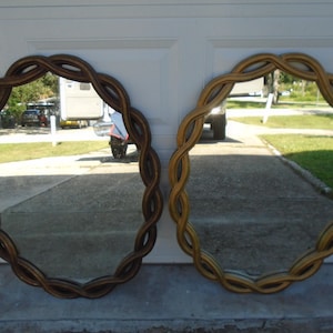 May include: Two oval mirrors with woven, rope-like frames. One mirror has a dark brown frame, the other a light brown frame. The mirrors reflect a driveway and a glimpse of the outdoors.