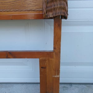 May include: A wooden headboard with a woven wicker top section. The headboard is constructed from light brown wood with a rectangular frame and a woven wicker panel. The wood has visible grain and knots.