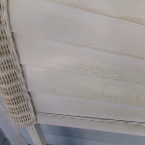 May include: Close-up of a section of a white painted wooden surface with horizontal planks. A woven wicker border is on the left side. The wood has a distressed, aged appearance.