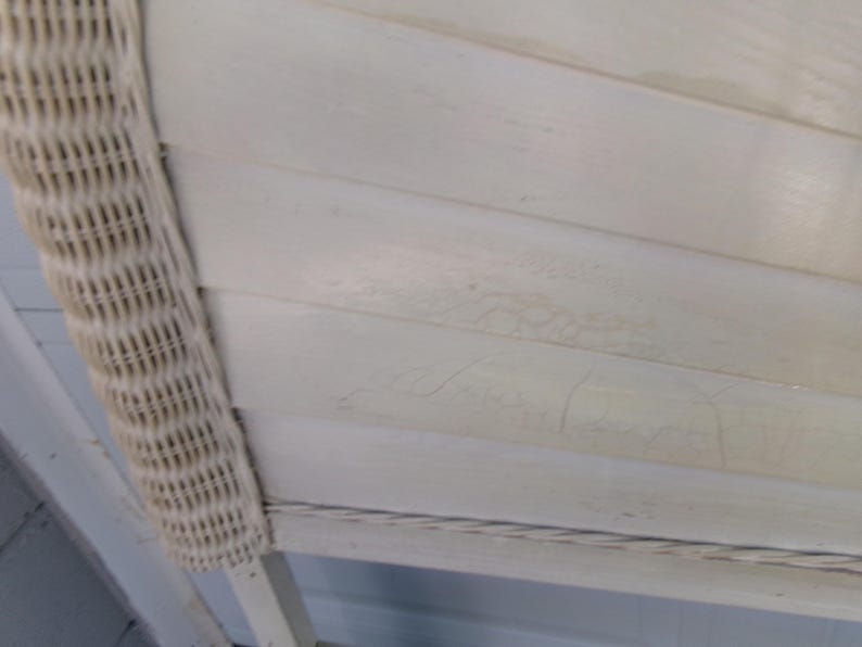 May include: Close-up of a section of a white painted wooden surface with horizontal planks. A woven wicker border is on the left side. The wood has a distressed, aged appearance.