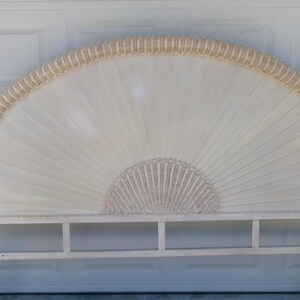May include: A white and beige fan-shaped headboard with a woven rattan border. The headboard has a rectangular base with a shelf. The design features a sunburst pattern, adding a touch of elegance to bedroom decor.
