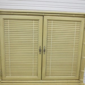 May include: A light green cabinet with two doors featuring faux bamboo detailing and horizontal slatted panels. The doors have brass handles.