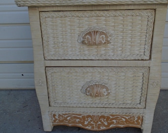 May include: A two-drawer wicker nightstand in a cream color. The drawers have decorative handles and are woven. The bottom of the nightstand has a decorative wood trim. The nightstand has a woven top.