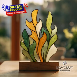May include: A stained glass pattern in the shape of stylized leaves, featuring shades of green, yellow, and orange, set on a wooden base. The design is labeled "DIGITAL PRODUCT STAINED GLASS PATTERN". The logo "AGV CRAFT Never Ending Craft" is also visible.