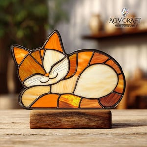 May include: A stained glass cat figurine in shades of orange, cream, and brown, resting on a wooden base. The cat is depicted in a relaxed pose with closed eyes and a smiling expression. The figurine has a black outline and the text "AGV Craft Never Ending Craft" is visible.