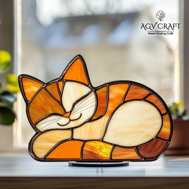 May include: A stained glass cat figurine in shades of orange, cream, and brown, with a black outline. The cat is depicted sleeping, with its eyes closed and a gentle smile. The figurine is on a black base, with the text "AGV CRAFT Never Ending Craft".