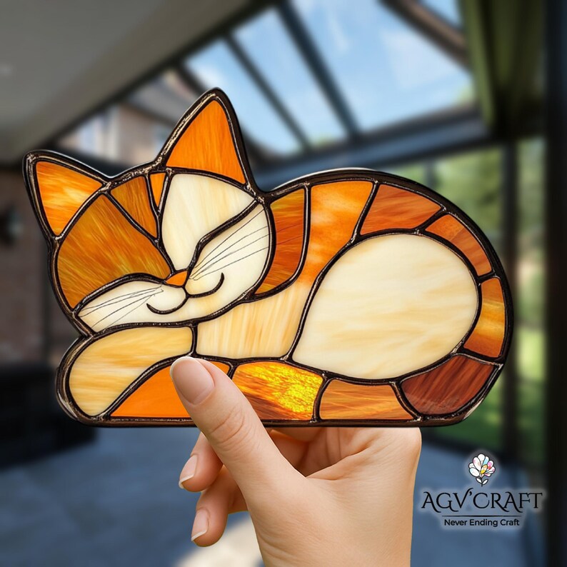 May include: A stained glass cat in shades of orange, cream, and brown, with a black outline. The cat is in a sleeping pose, with its eyes closed and a gentle smile. The image is of a decorative item.