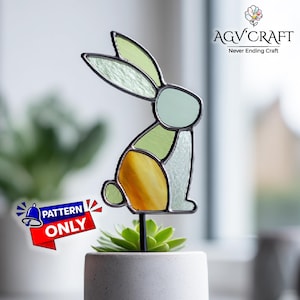 May include: A stained glass rabbit garden stake in shades of green, yellow, and clear glass. The rabbit is mounted on a black metal stake and is placed in a small white pot with a succulent plant. The image includes the text "PATTERN ONLY".