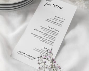 Puede incluir: Un menú de boda en blanco y negro con el título "The Menu" en la parte superior. El menú enumera las opciones de aperitivos, plato principal y postre. La parte inferior del menú incluye los nombres Allison & Matthew y la fecha 02.14.25. El menú está sobre una superficie blanca con pequeñas flores rosas.