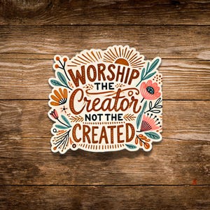 May include: A sticker with the text "Worship the Creator not the Created" in a decorative font. The sticker has a cream-colored background with floral and leaf accents in shades of orange, pink, and teal. A sunburst design is at the top.
