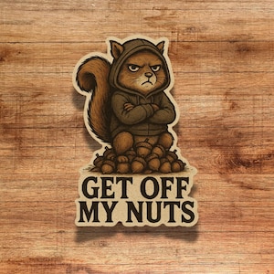 May include: A sticker featuring a cartoon squirrel wearing a hoodie and standing on a pile of acorns. The squirrel has a stern expression with arms crossed. The text "GET OFF MY NUTS" is below the squirrel.
