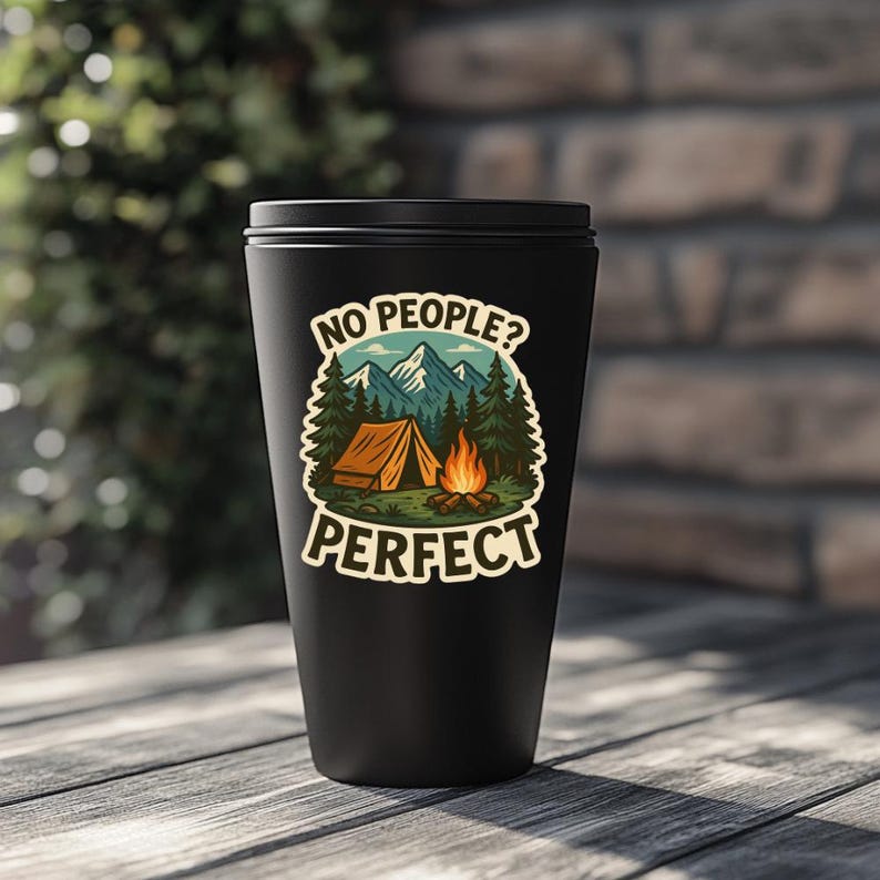 May include: Black travel mug with a sticker that says "No people? Perfect." The sticker features a cartoon illustration of a campsite with a tent, trees, mountains, and a campfire.