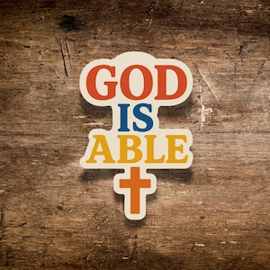 May include: A sticker with the words "GOD IS ABLE" in red, blue, and yellow, with a cross at the bottom. The sticker is on a wooden surface.