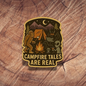 May include: A sticker with a camping theme. It features a Bigfoot roasting a marshmallow over a campfire, with a tent, mountains, and a crescent moon in the background. The text "Campfire Tales Are Real" is at the bottom.