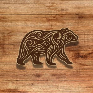 May include: A brown bear silhouette with intricate floral and nature-inspired patterns. The bear is walking to the right and has a stylized design.