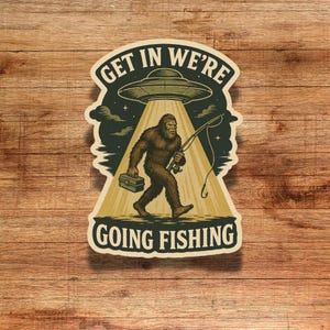 May include: A sticker featuring a Bigfoot character walking towards a UFO, holding a fishing rod and tackle box. The text reads "GET IN WE'RE GOING FISHING" in a vintage style.