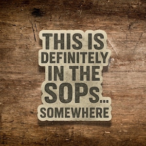 May include: A rectangular sticker with the text "THIS IS DEFINITELY IN THE SOPS... SOMEWHERE" in a bold, distressed font. The sticker has a textured, off-white appearance and is set against a wooden background.