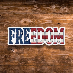 May include: A rectangular sticker with the word "FREEDOM" in bold, patriotic colors. The letters "F-R-E-E" are blue with white stars, and the letters "D-O-M" are red and white stripes, set against a wooden background.