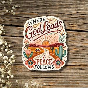 May include: A sticker with a sunset scene and the text "Where God Leads Peace Follows". The sticker features a road leading into the sunset with a car driving on it. There are cacti and flowers on either side of the road.