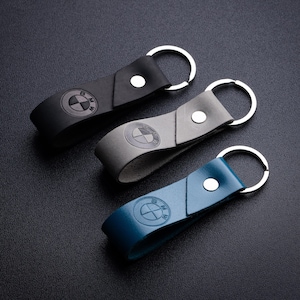 May include: Three leather keychains with silver key rings. The keychains are black, gray, and blue. Each keychain features a silver BMW logo.