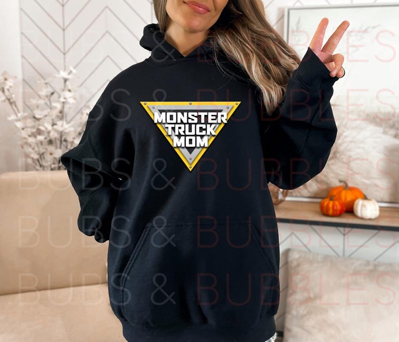 Puede incluir: Sudadera con capucha negra con bolsillo delantero y el texto "MONSTER TRUCK MOM" en un dise&ntilde;o triangular amarillo y blanco. La sudadera es de estilo casual.
