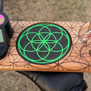 Puede incluir: Una bandeja de madera con un patrón geométrico y un dispositivo negro con una pantalla y una parte superior rosa y verde. La bandeja tiene un diseño de círculo verde y varias canicas de vidrio.